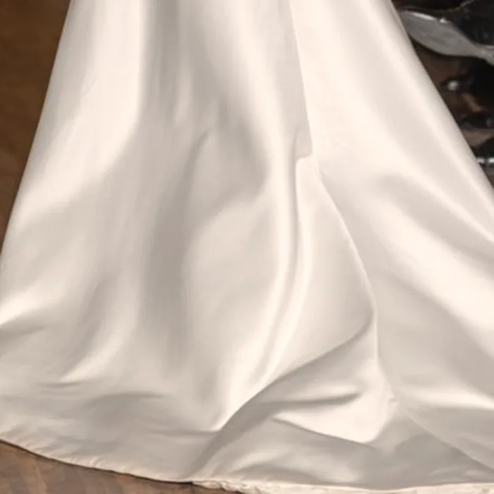 Pieghe scultoree in mikado di seta di una gonna da sposa, dettaglio ravvicinato